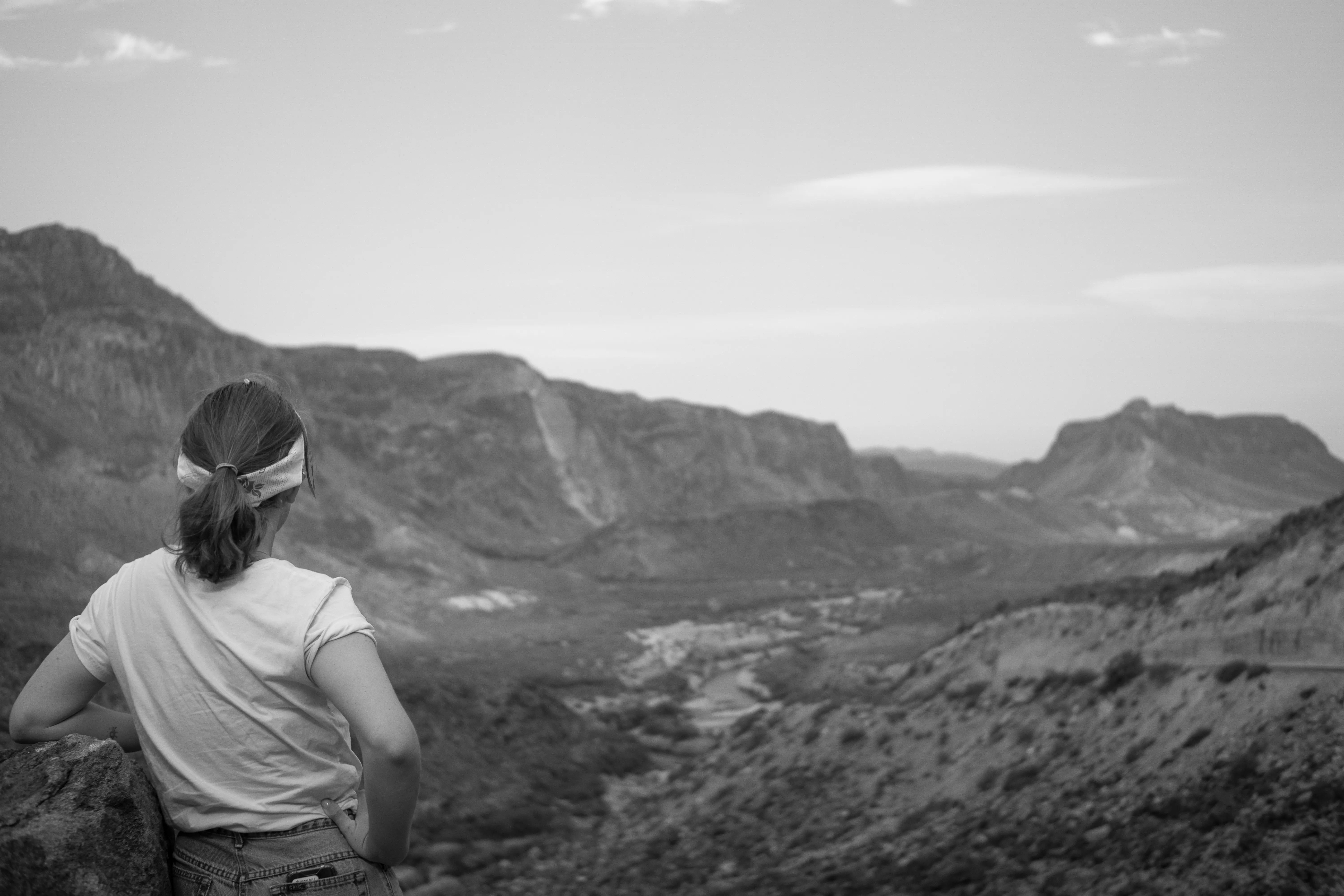 A woman leaning her elbow on a rock look down into a valley.