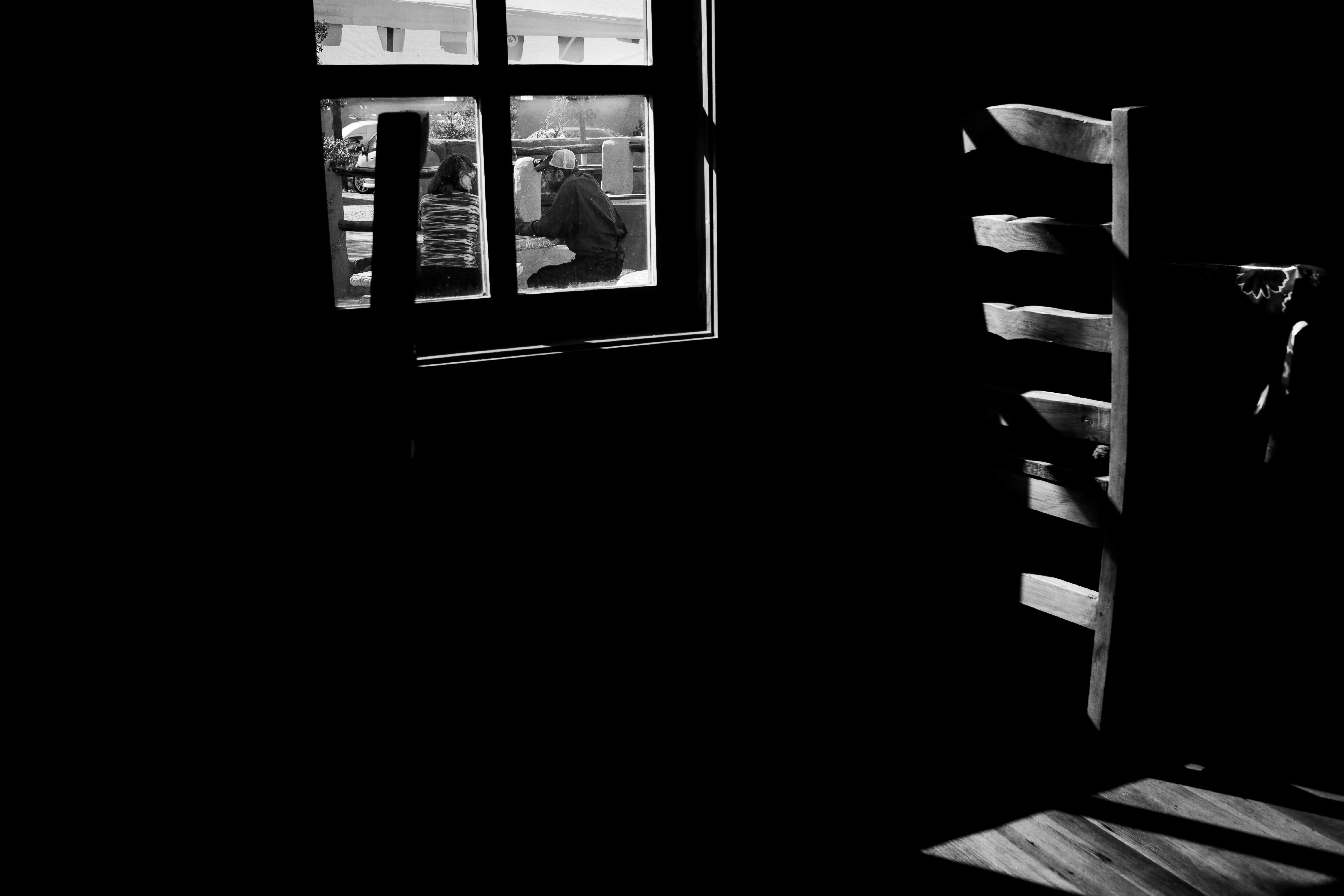 A chair next to a window with a man and woman sitting outside.