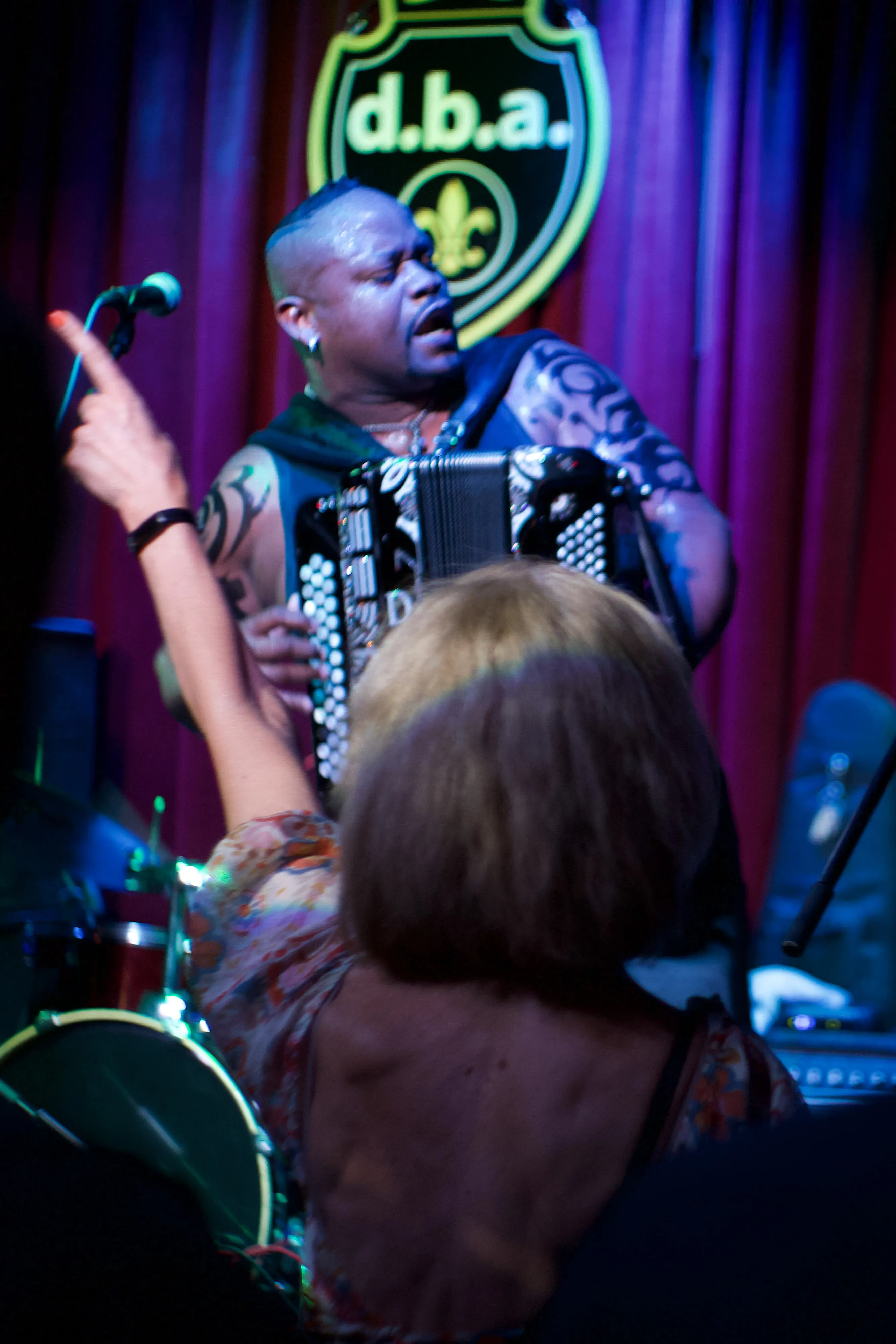 A woman raising her hand in front of Dwayne Dopsie as he plays the accordion.