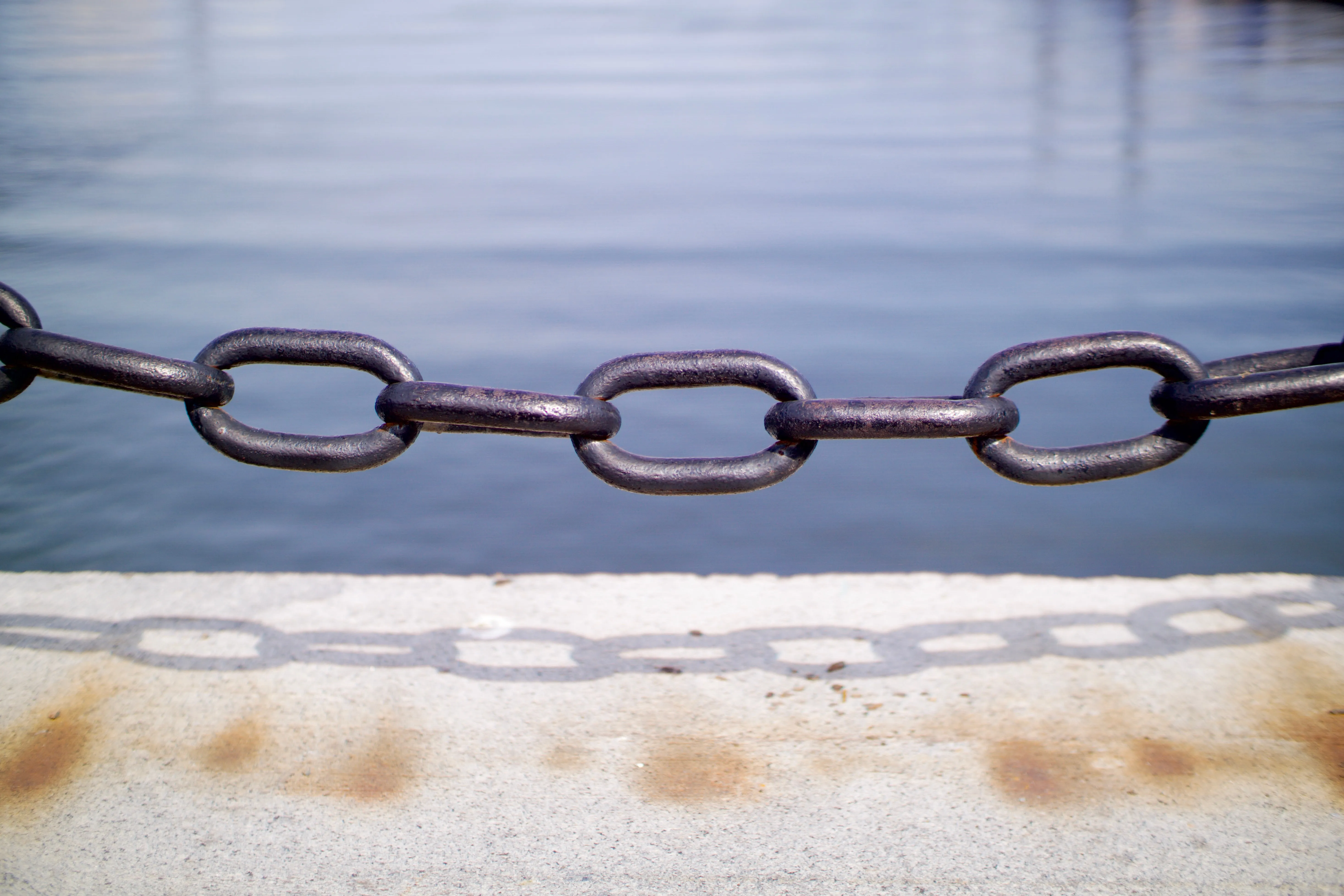 A heavy chain hanging across a cement barrier next to a harbor.