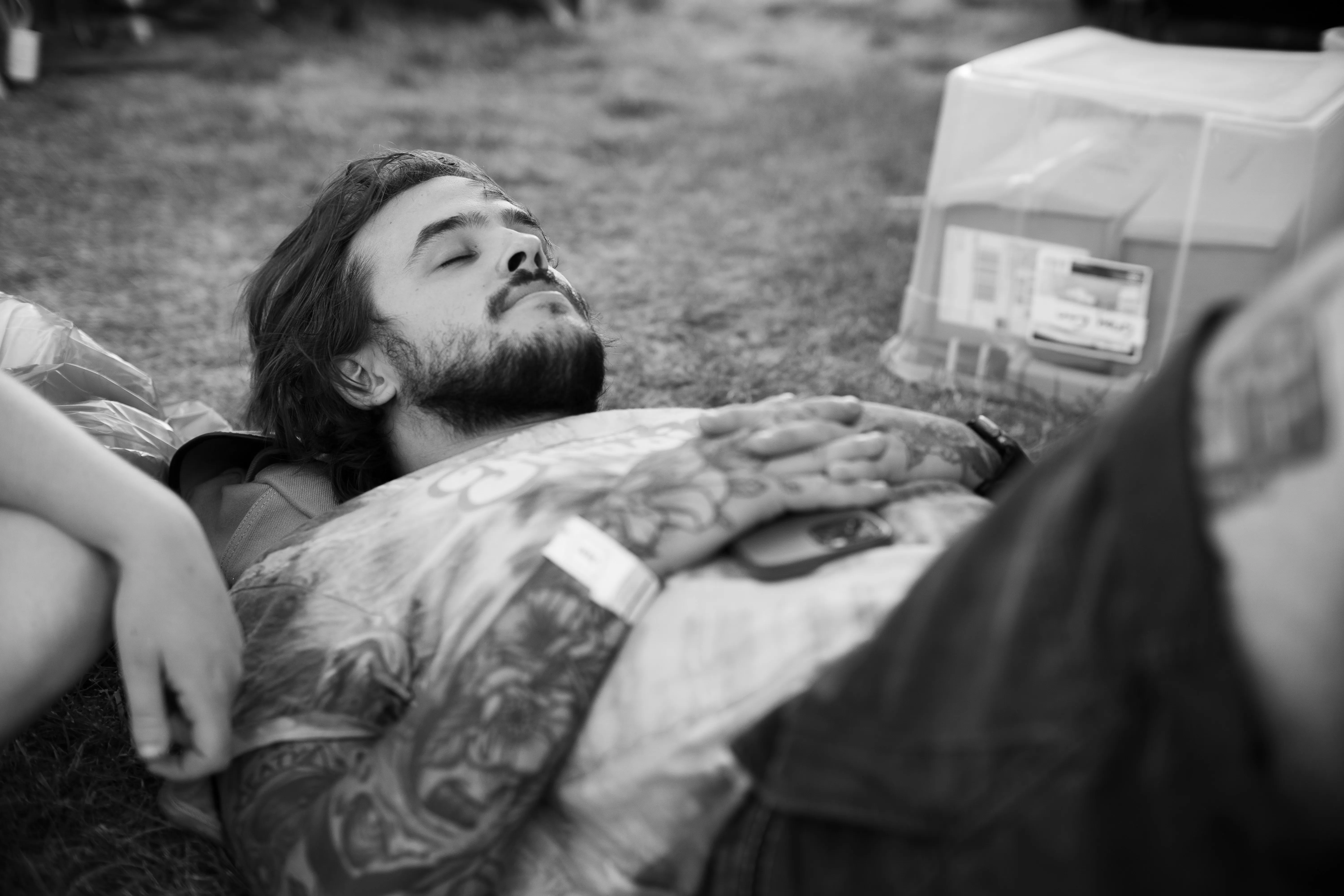 A man taking a nap in a park, using his backpack as a pillow.