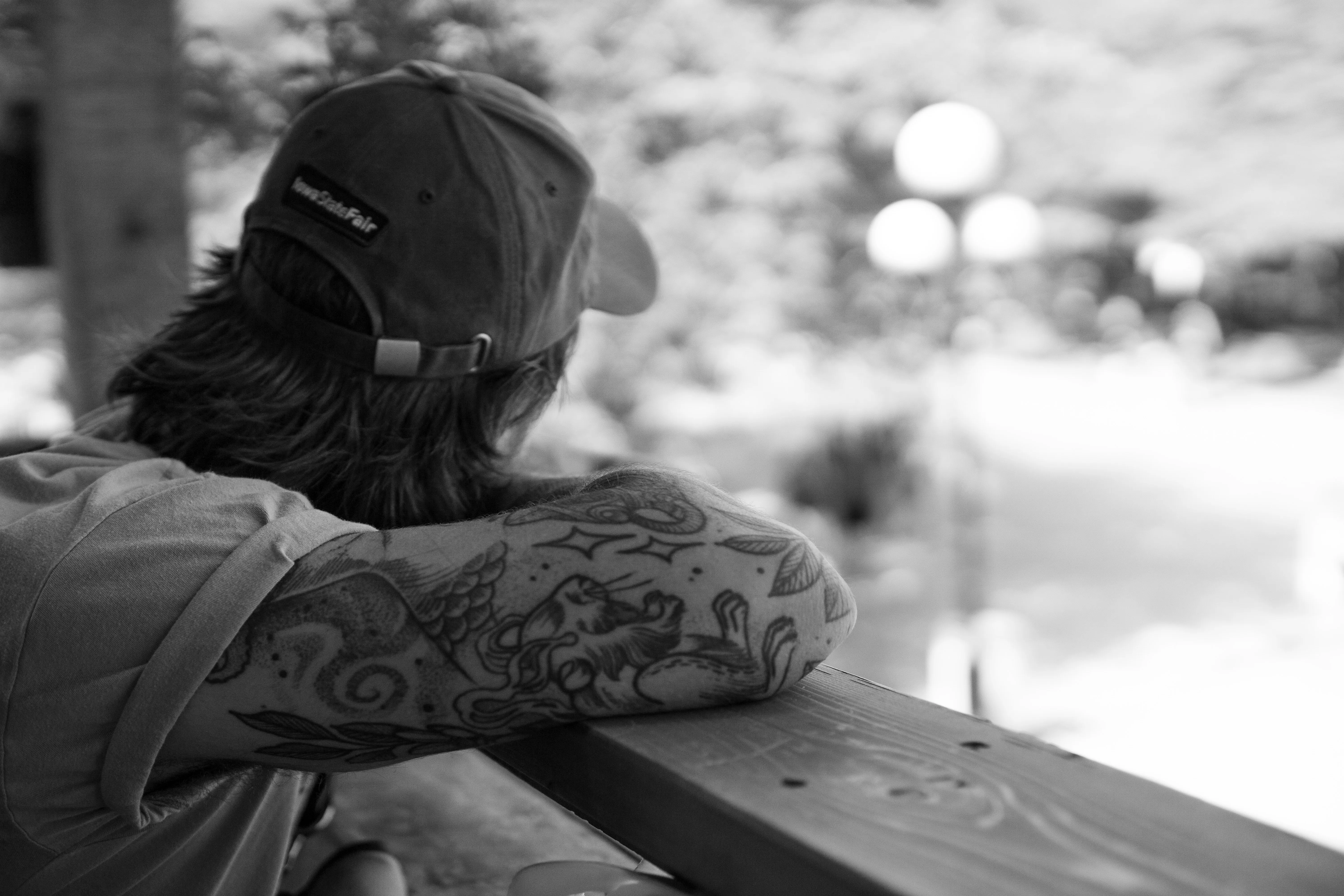 A man with tattooed arms leaning on a balcony railing.