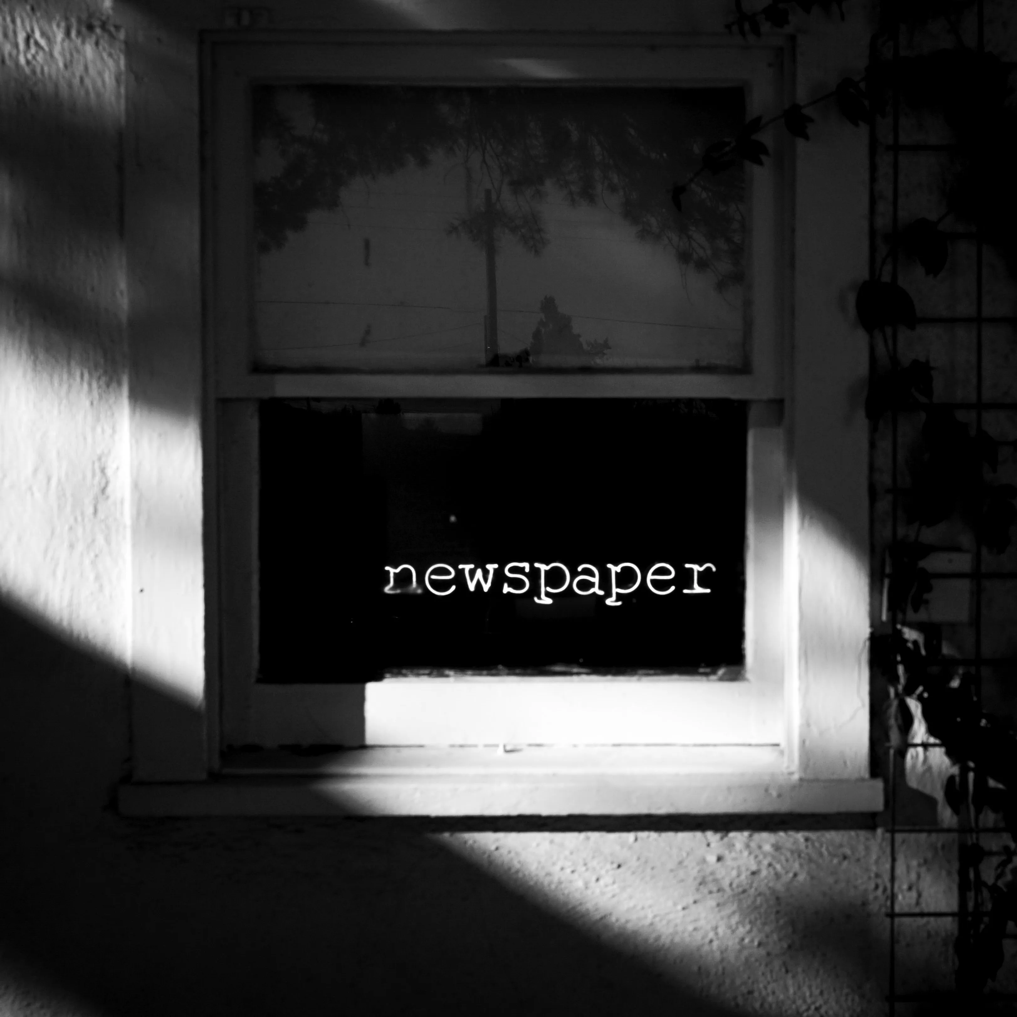 A black and white photo of a neon sign in a window that reads "newspaper."