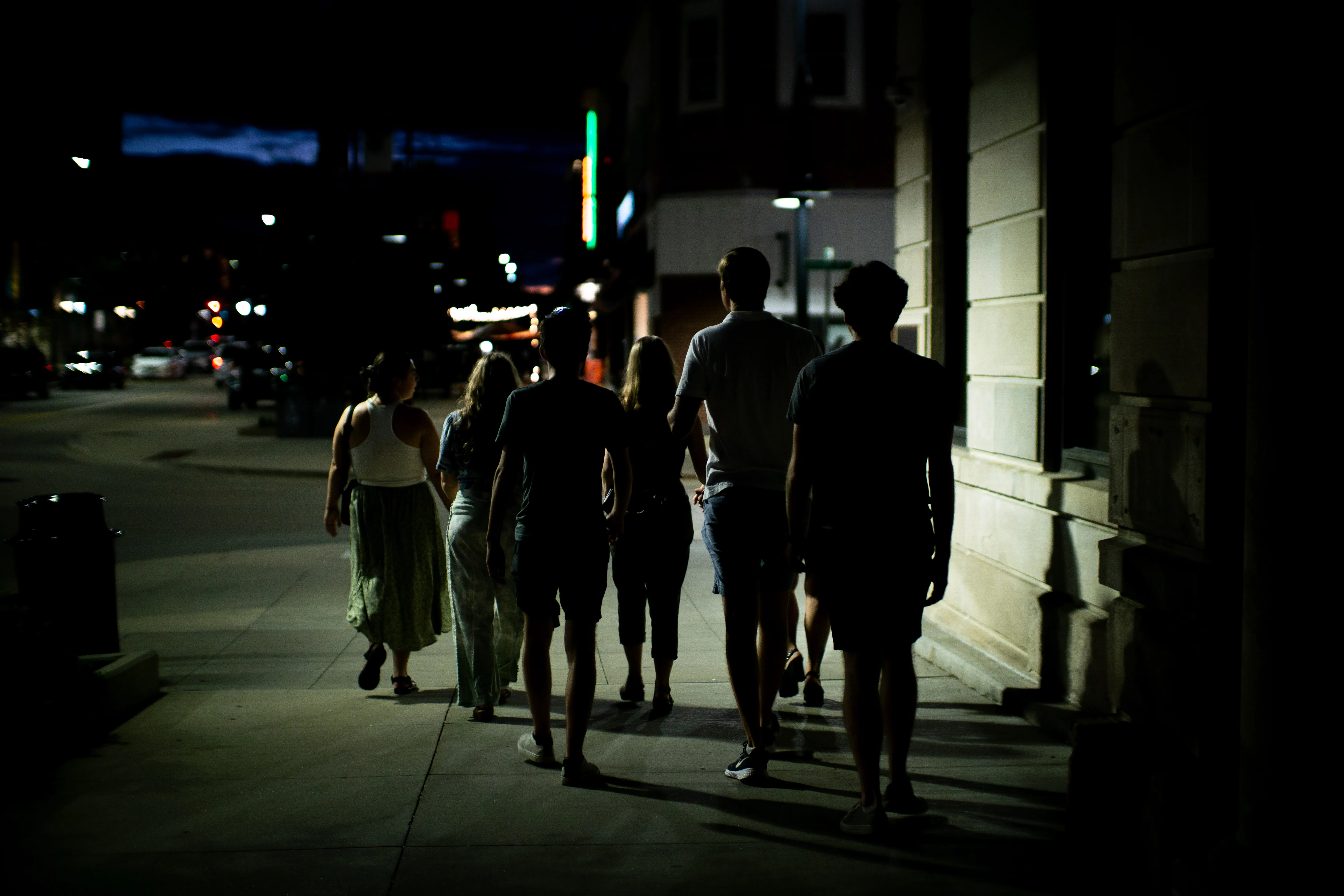 A group of young people walking on a sidewalk at night.