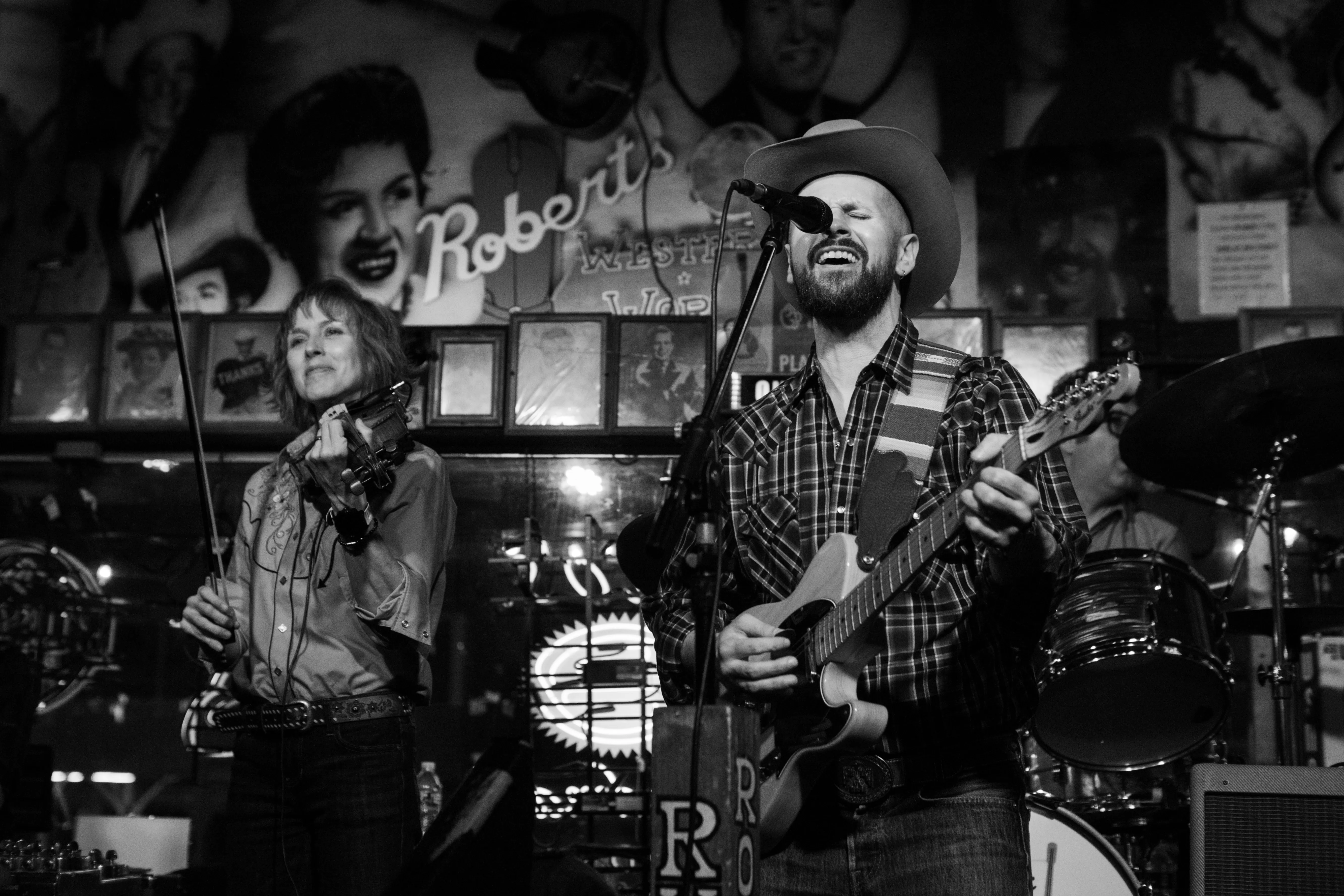 A singer singing into a microphone and playing guitar at Robert's Western World.