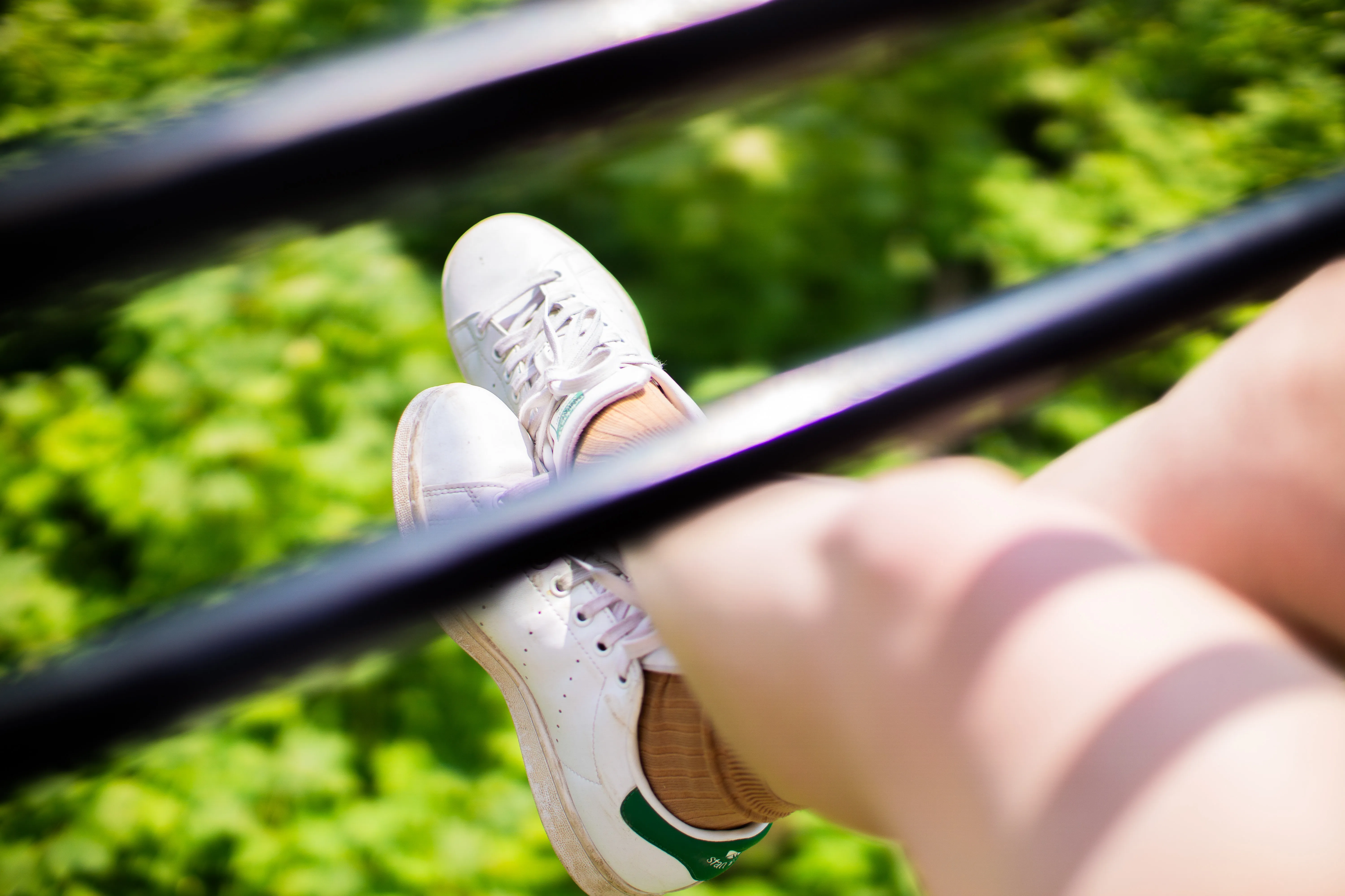 A woman's legs and sneakers on a skyglider dangling over trees.