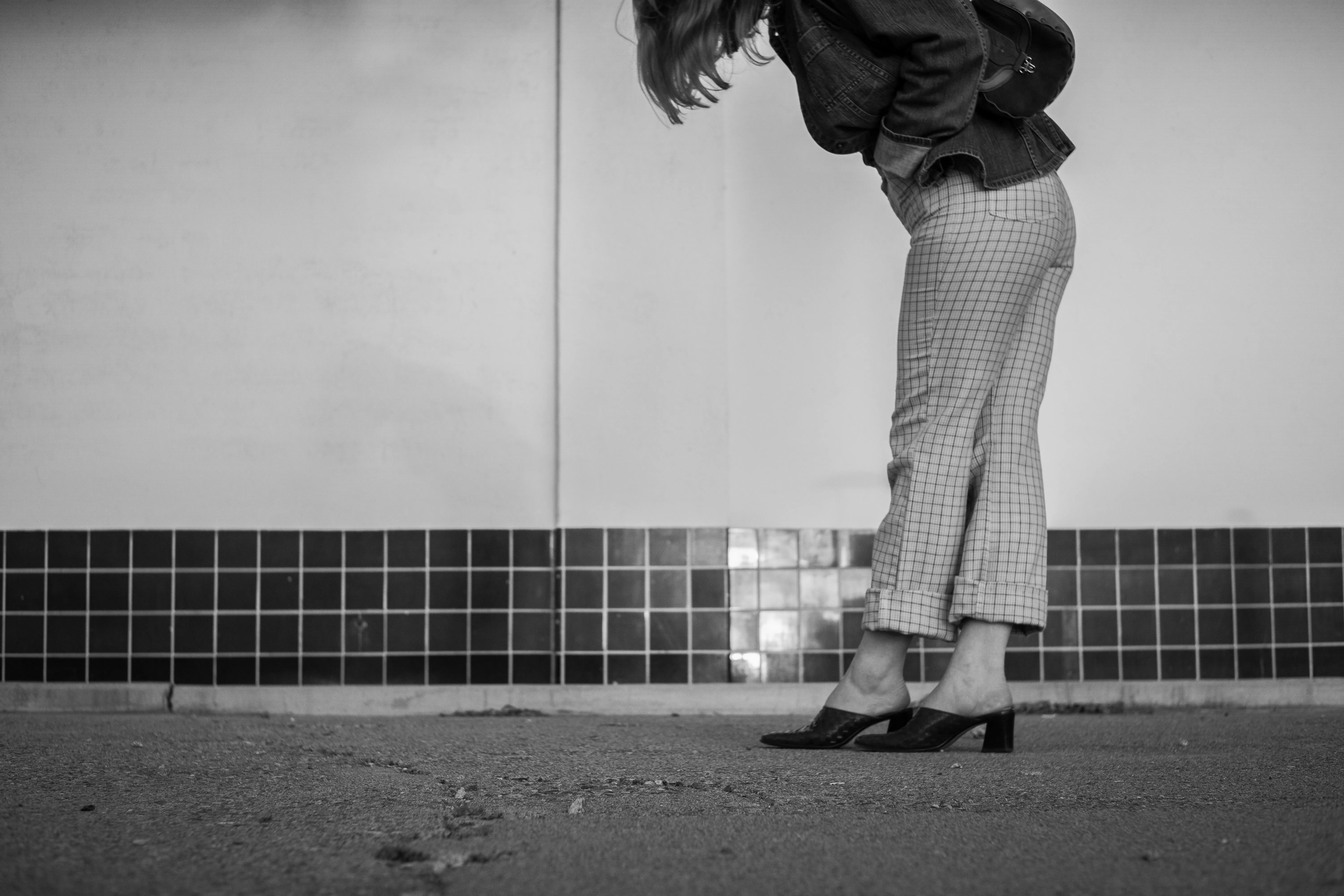 A black and white shot of a woman from the shoulders down, wearing plaid pants and leather shoes.