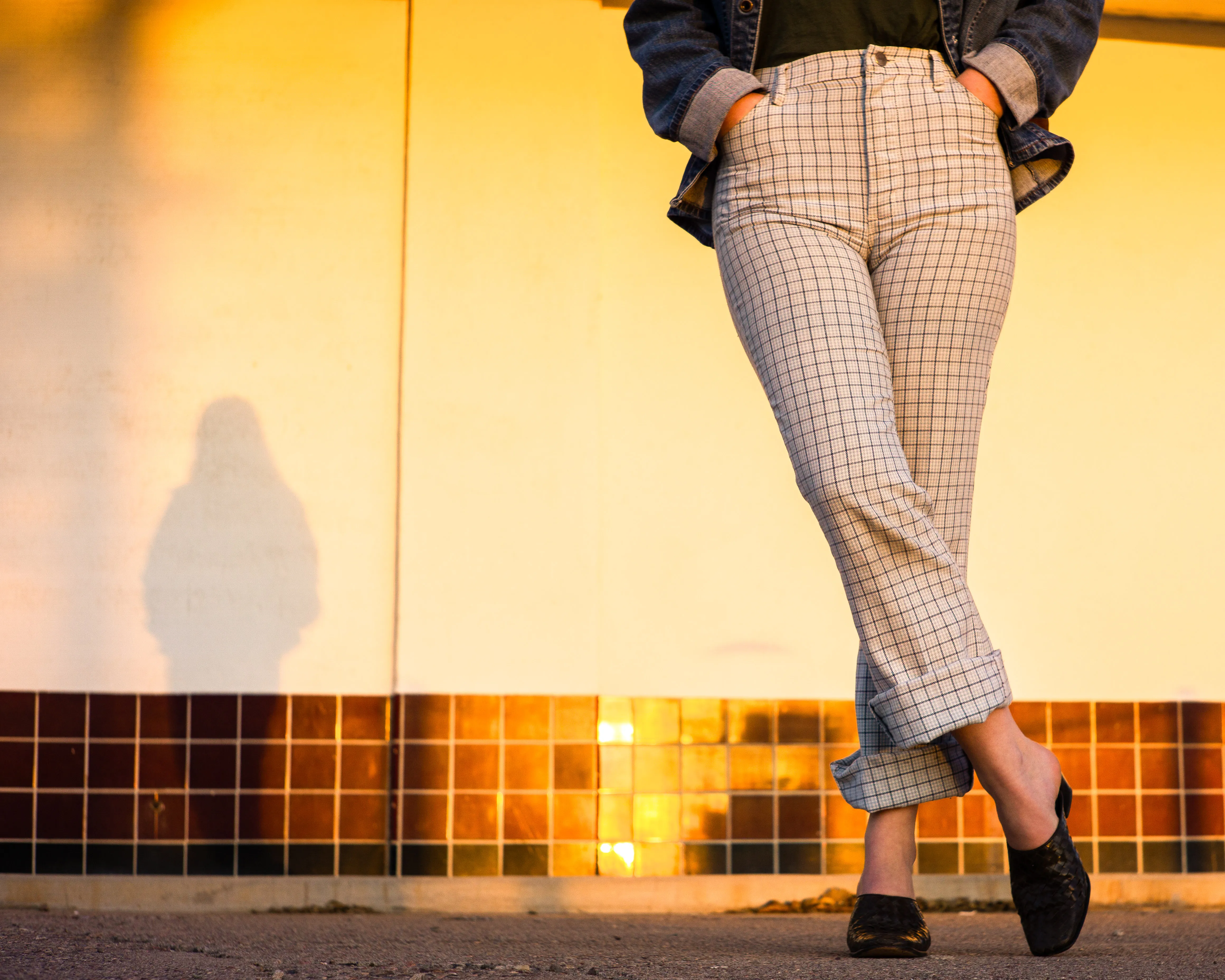 A woman from the waist down, wearing plaid pants and leather shoes.